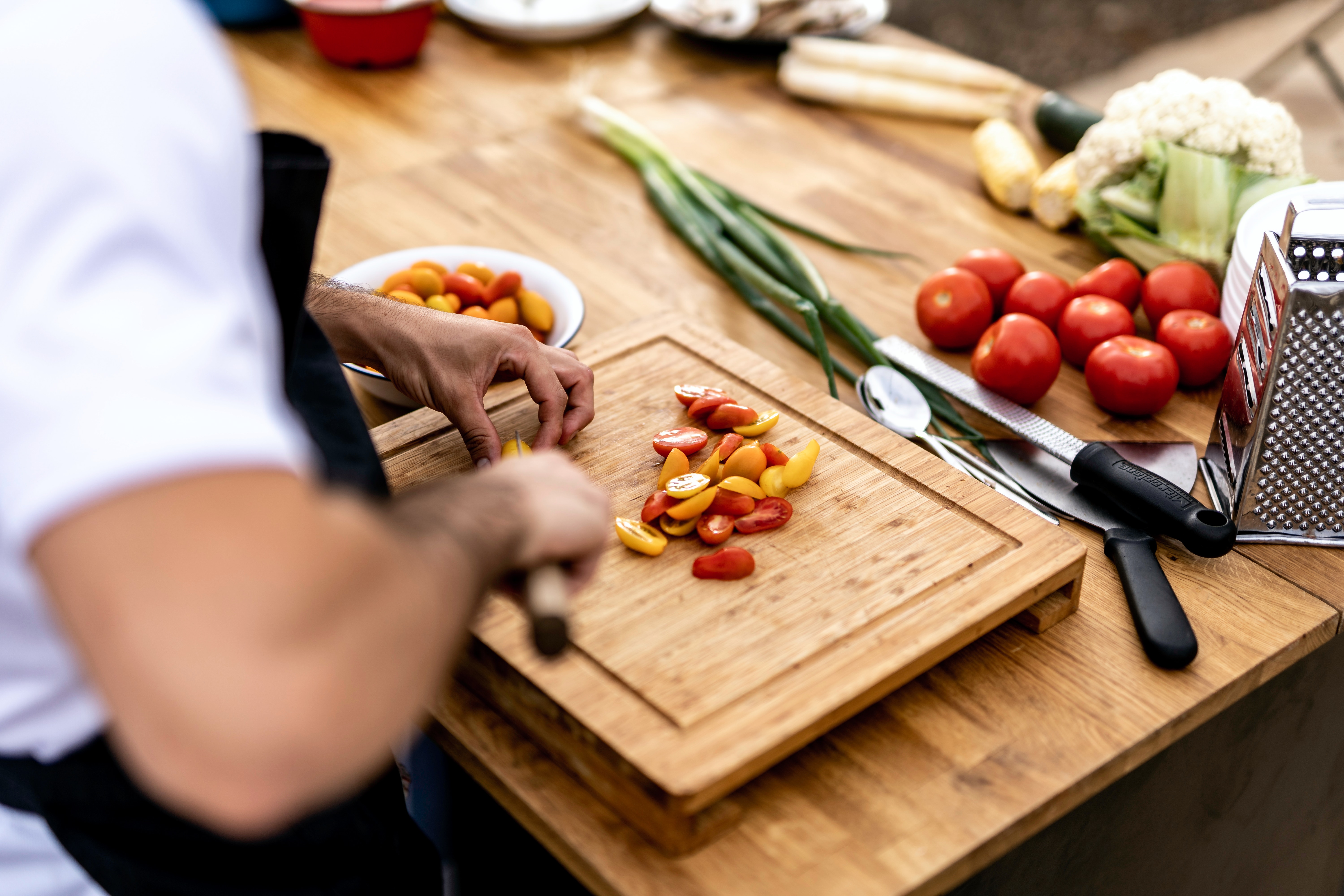 Man dicing cherry tomatoes with a knife on a wooden chopping board. 